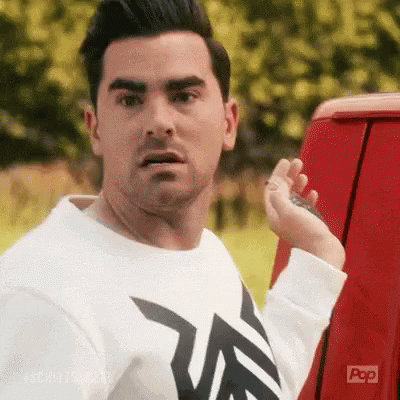 A Man In A White Shirt Is Standing Next To A Red Van And Holding A Key . GIF