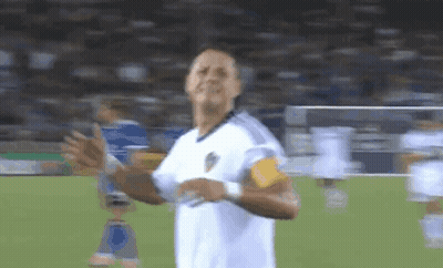 A Man In A White Shirt Is Standing On A Soccer Field With His Hands In The Air GIF