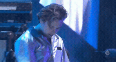 A Man In A White Shirt Is Standing On A Stage In Front Of A Blue Light . GIF