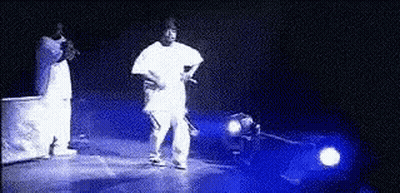 A Man In A White Shirt Is Standing On A Stage In Front Of A Car . GIF