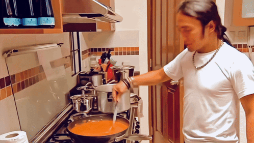 A Man In A White Shirt Is Stirring A Pot Of Soup GIF