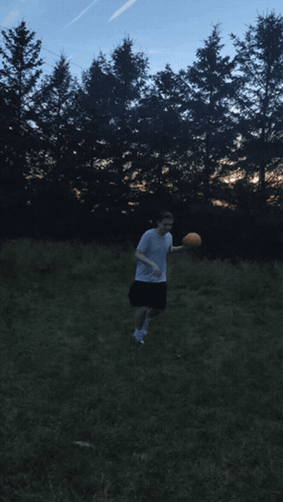 A Man In A White Shirt Is Throwing A Frisbee In A Field With Trees In The Background GIF