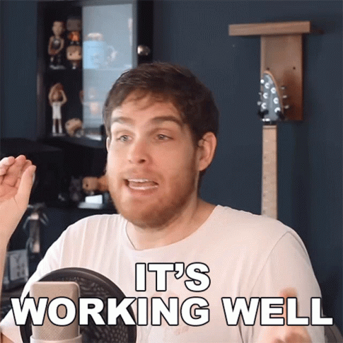 A Man In A White Shirt Says It 'S Working Well In Front Of A Microphone GIF