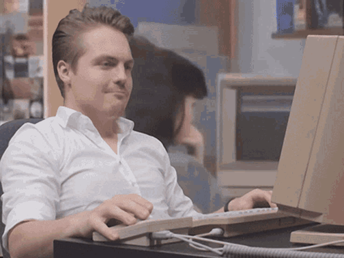 A Man In A White Shirt Sits In Front Of A Computer GIF