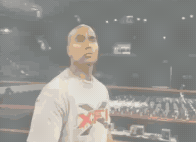 A Man In A White Shirt Stands In A Dark Room GIF