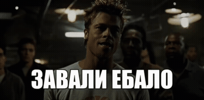 A Man In A White Shirt Stands In A Dark Room With The Words " Завали Ебалo " Above Him GIF