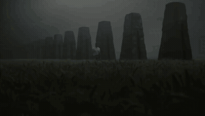 A Man In A White Shirt Stands In A Field With A Row Of Stones In The Background GIF