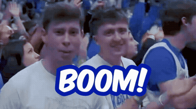 A Man In A White Shirt Stands In Front Of A Blue Sign That Reads Boom GIF