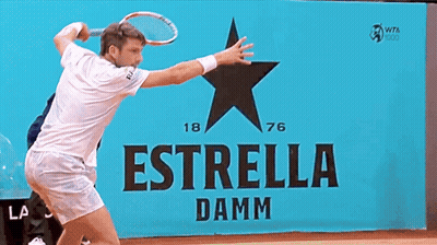 A Man In A White Shirt Stands In Front Of A Sign That Says Estrella Damm GIF