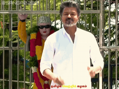 A Man In A White Shirt Stands In Front Of A Statue Of A Woman In A Yellow And Red Outfit GIF