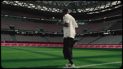 A Man In A White Shirt Stands On A Soccer Field In Front Of A Stadium That Says Stadium Tour GIF