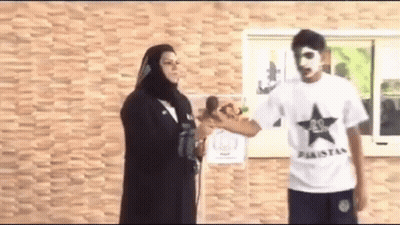 A Man In A White Shirt With A Black Star On It Is Standing Next To A Woman In A Black Hijab . GIF