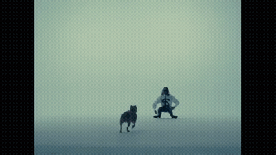A Man In A White Shirt With A Cross On It Stands Next To A Dog GIF