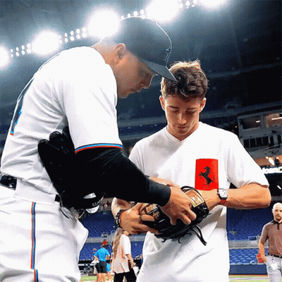 A Man In A White Shirt With A Ferrari Logo On It Talks To Another Man GIF