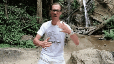 A Man In A White Shirt With The Word Metafyme On It Is Running In Front Of A Waterfall GIF