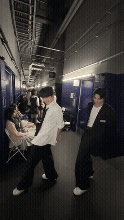 A Man In A White Shirt With The Word Nct On It Stands In A Hallway GIF