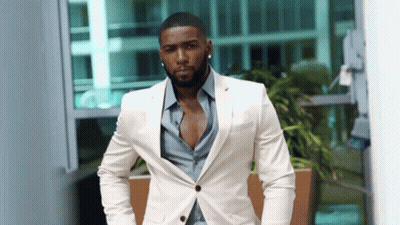 A Man In A White Suit And Blue Shirt Is Standing In Front Of A Building GIF