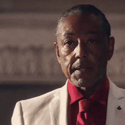 A Man In A White Suit And Red Tie Is Looking At The Camera GIF