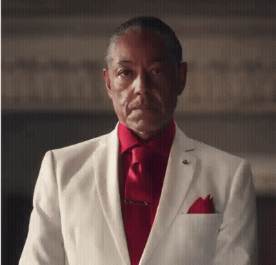 A Man In A White Suit And Red Tie Looks At The Camera GIF