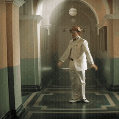 A Man In A White Suit And Straw Hat Is Dancing In A Hallway GIF