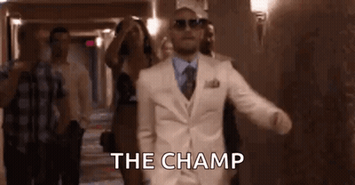 A Man In A White Suit And Sunglasses Is Walking Down A Hallway With A Group Of People . GIF