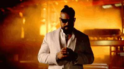 A Man In A White Suit And Sunglasses Stands In Front Of A Fire GIF