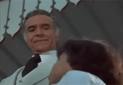 A Man In A White Suit And Tie Is Kissing A Woman . GIF