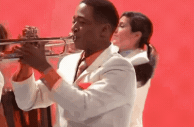 A Man In A White Suit And Tie Is Playing A Trumpet GIF