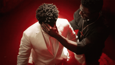 A Man In A White Suit Is Being Touched By Another Man In A Black Shirt GIF