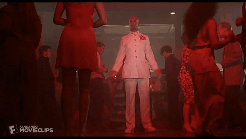 A Man In A White Suit Is Dancing In Front Of A Crowd Of People With The Word Movieclips On The Bottom Left GIF