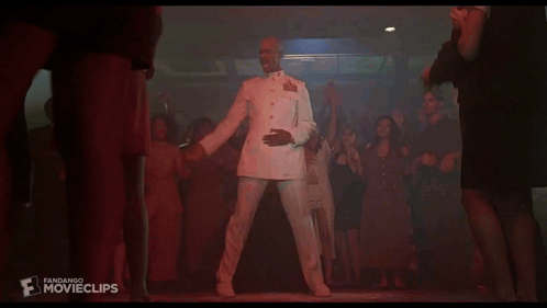A Man In A White Suit Is Dancing In Front Of A Crowd Of People With The Word Movieclips On The Bottom GIF