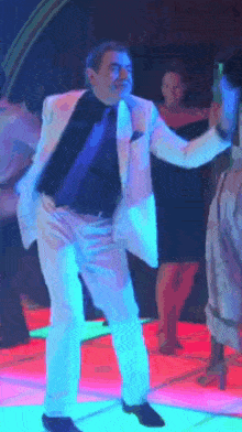 A Man In A White Suit Is Dancing On A Neon Dance Floor GIF