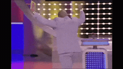 A Man In A White Suit Is Dancing On A Stage With His Arms Outstretched . GIF