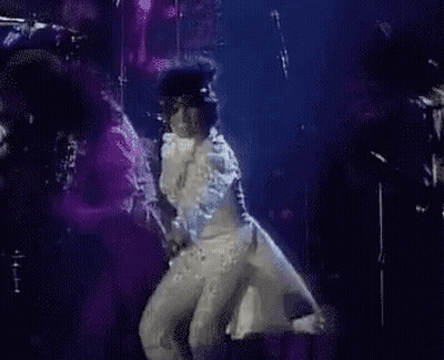 A Man In A White Suit Is Dancing On A Stage . GIF