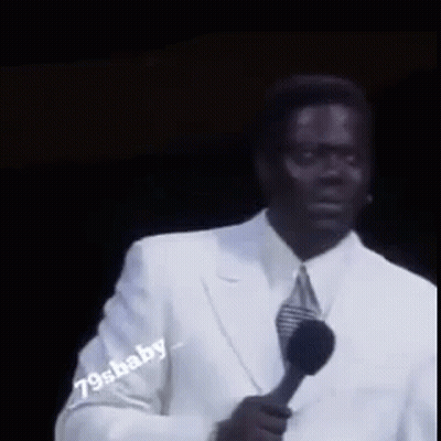 A Man In A White Suit Is Holding A Microphone In His Hand . GIF