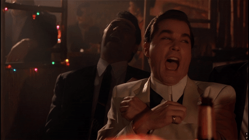 A Man In A White Suit Is Laughing With Another Man In A Black Suit Behind Him GIF