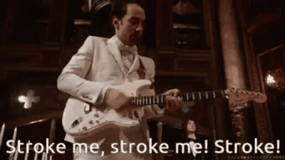 A Man In A White Suit Is Playing A Guitar In A Room . GIF