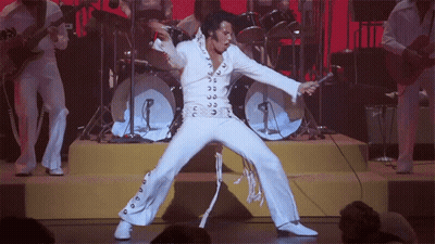 A Man In A White Suit Is Singing Into A Microphone On A Stage GIF