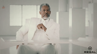 A Man In A White Suit Is Sitting At A Table With Regal Written On The Bottom GIF