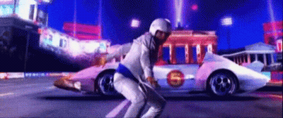 A Man In A White Suit Is Squatting In Front Of A Race Car With The Letter S On The Side . GIF