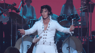 A Man In A White Suit Is Standing In Front Of A Drum Set On A Stage GIF