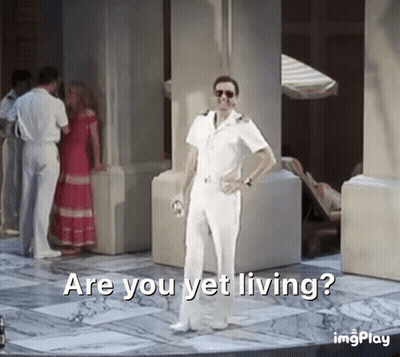 a man in a white suit is standing in front of a group of people and says are you yet living