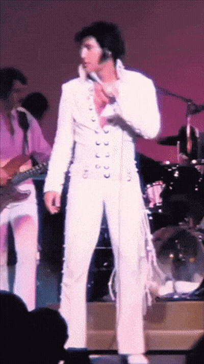 A Man In A White Suit Is Standing In Front Of A Microphone GIF