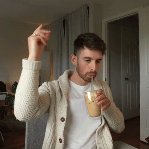 A Man In A White Sweater Drinking Through A Straw GIF