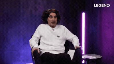A Man In A White Sweater Is Sitting In A Chair In Front Of A Purple Background With Legend Written On It GIF