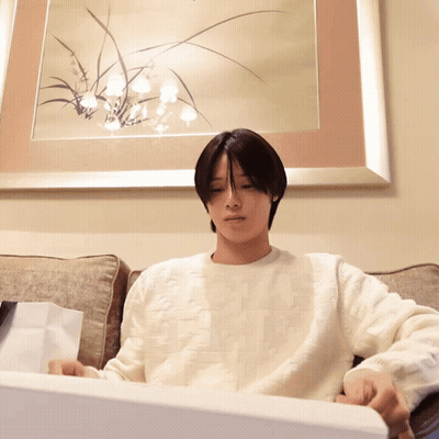 A Man In A White Sweater Is Sitting On A Couch In Front Of A Picture GIF