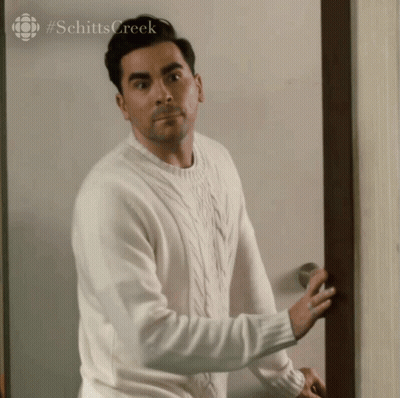 A Man In A White Sweater Is Standing In Front Of A Door . GIF
