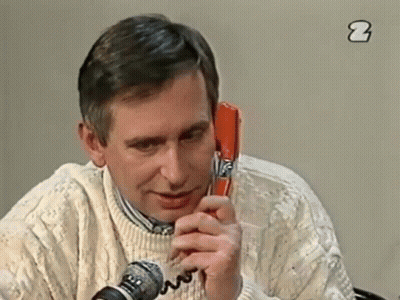 A Man In A White Sweater Is Talking On A Red Telephone GIF
