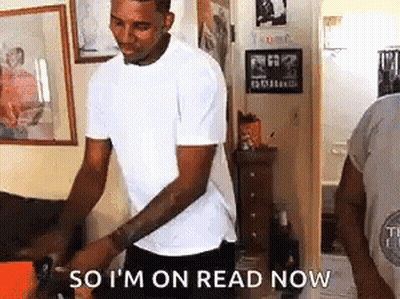 A Man In A White T-Shirt Is Standing In A Living Room Holding A Box . GIF