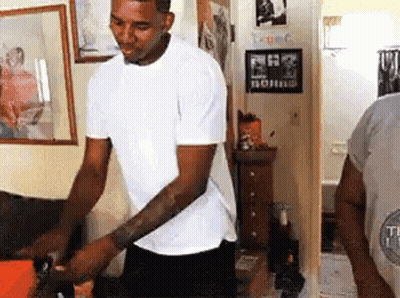A Man In A White T-Shirt Is Standing In A Room . GIF